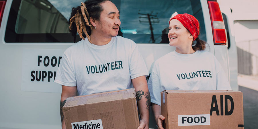 a man and a woman wearing volunteer white tshirts carrying boxes at the back of a white van